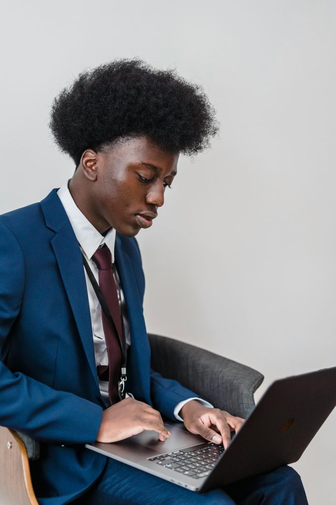A young man in a blue suit using a laptop indoors, focused on work.